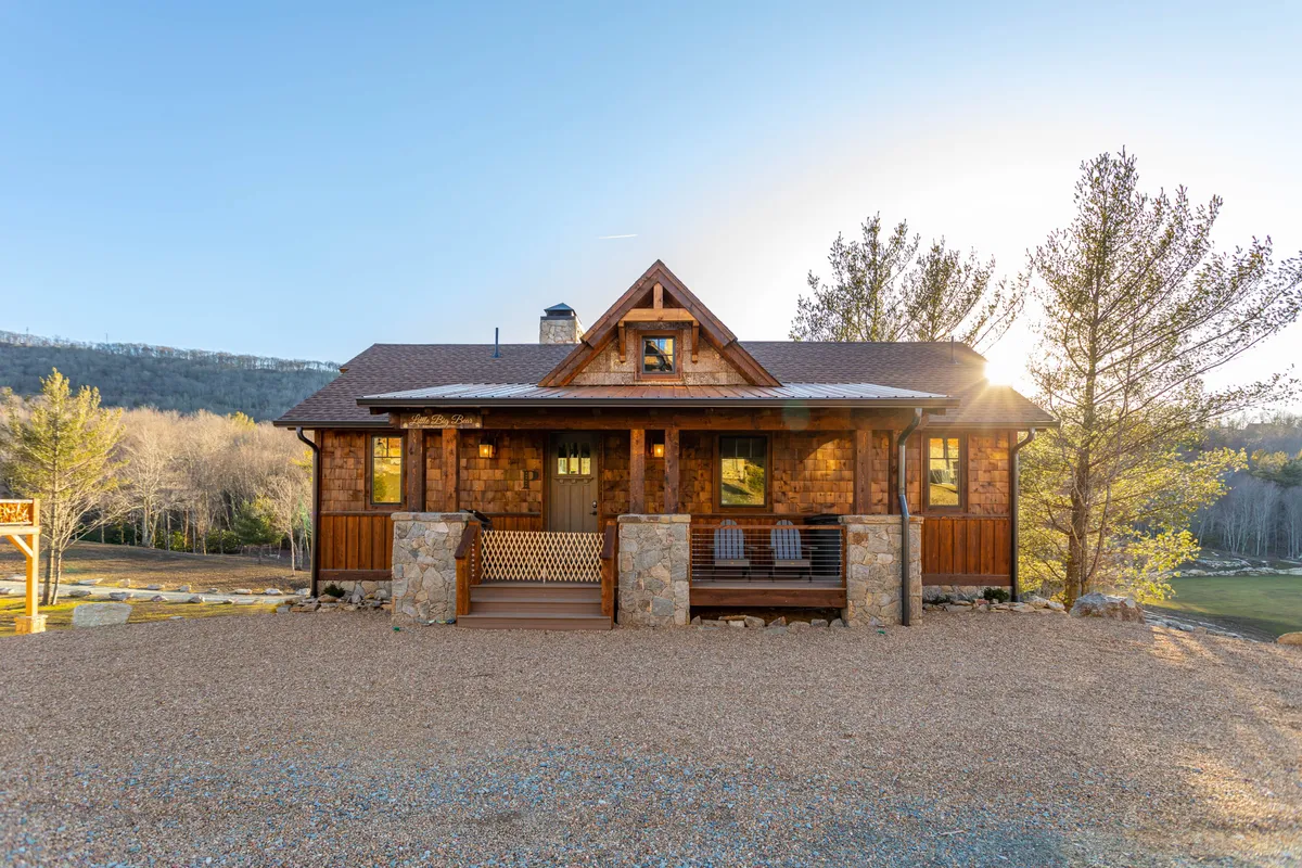 This image features the inviting wooden facade of the home, with stone steps leading up to a porch that offers comfortable seating. The large windows reflect a sweeping mountain backdrop, setting an adventurous tone, while the porch signals a launch point for outdoor activities like nature walks or relaxing after a day on the trails.