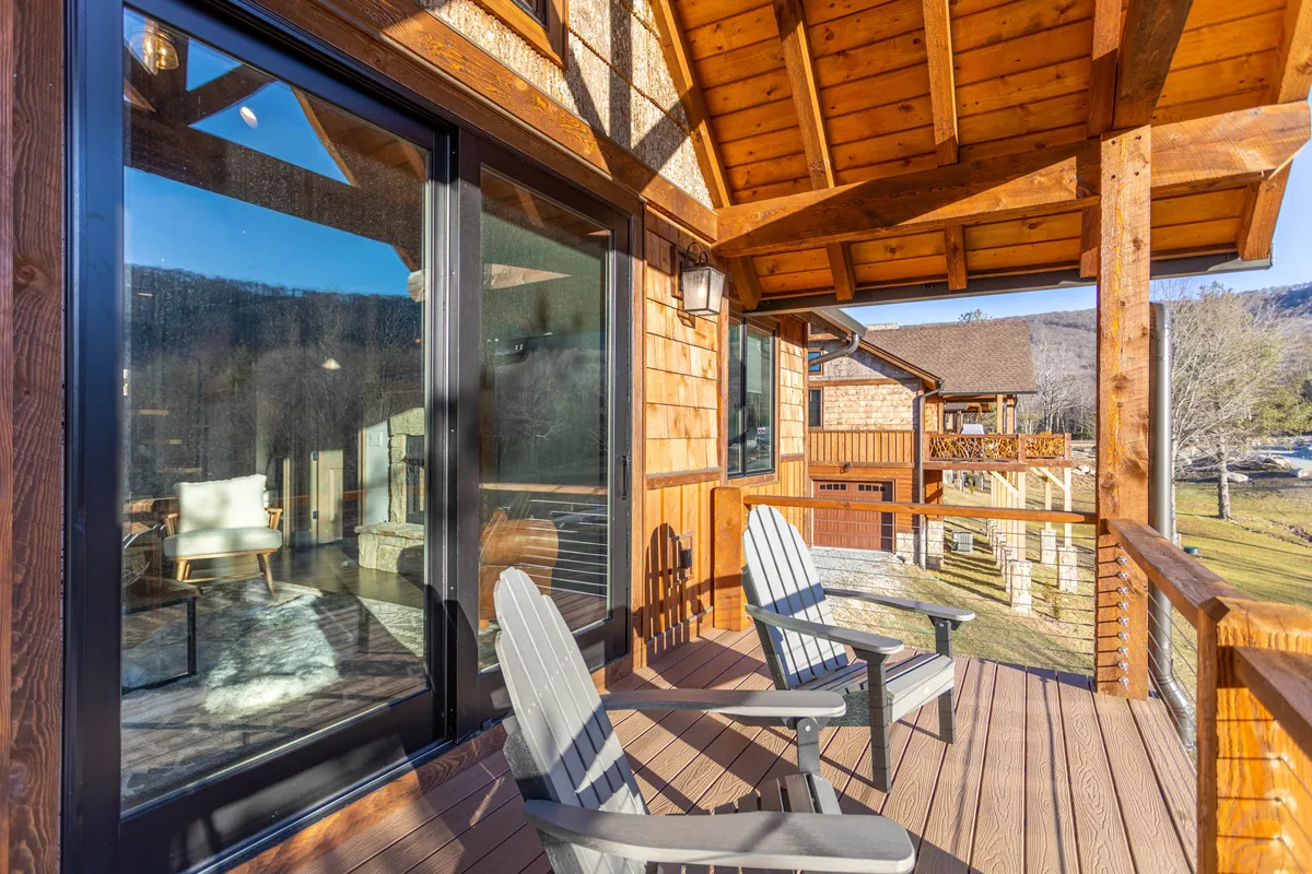 This image features a wooden deck outfitted with classic Adirondack chairs, overlooking a tranquil mountain view through large windows. The setting is serene, offering a direct connection to the outdoors and a perfect vantage point for enjoying the natural scenery at any time of day.
