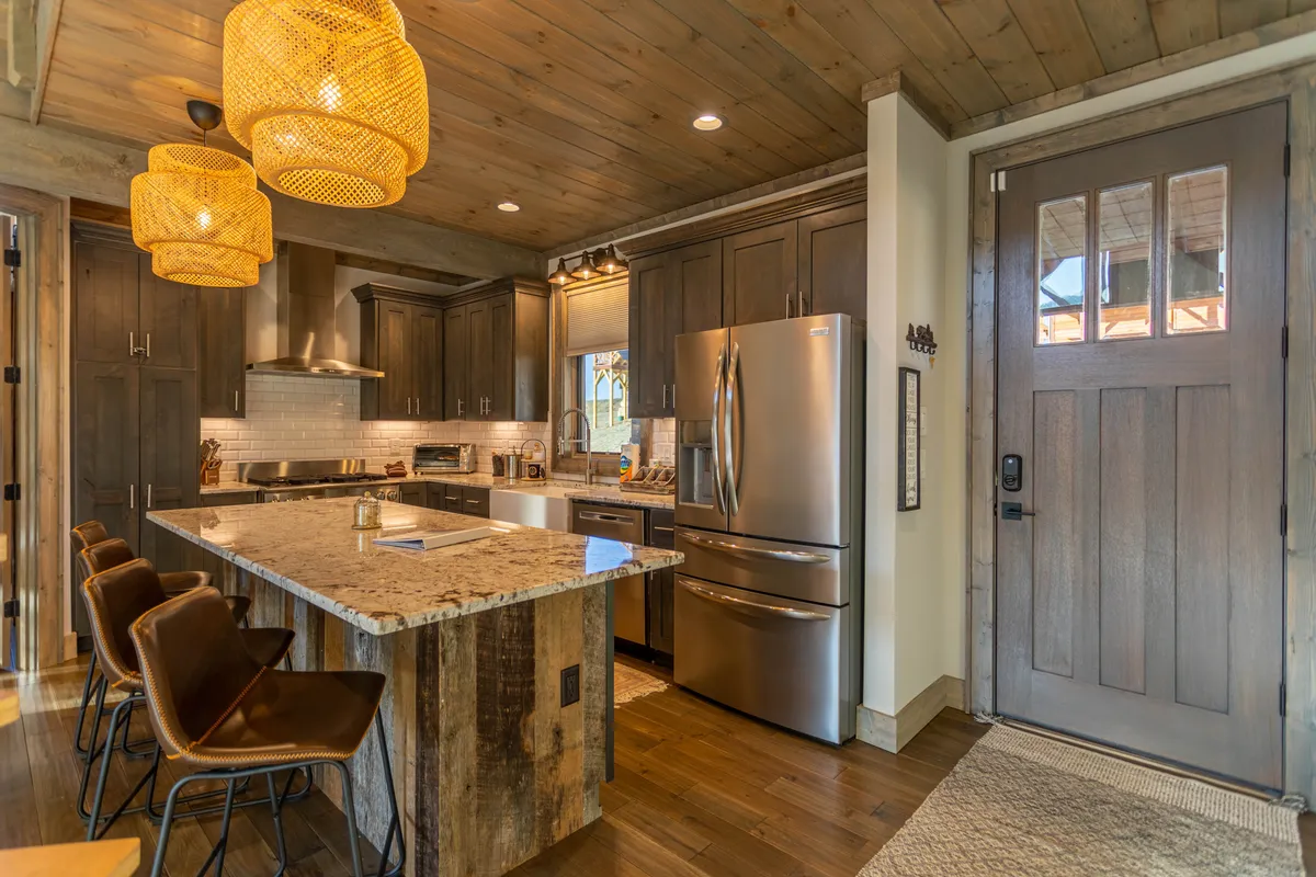 A bright, open kitchen featuring a large granite island with hanging pendant lights, stainless steel appliances including a gas stove, and warm wooden cabinetry. The layout encourages interaction with a spacious bar area for seating, perfect for socializing while cooking.
