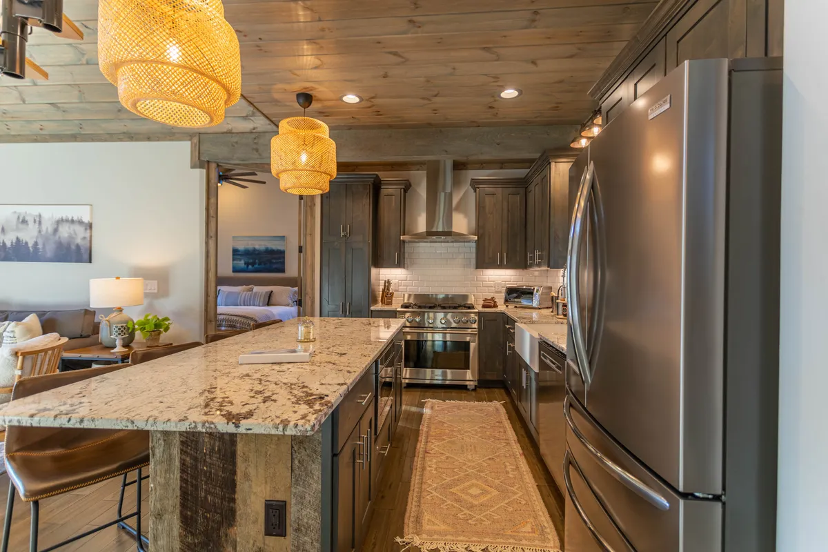 A spacious, modern kitchen with a large granite island, pendant lighting, and stainless steel appliances. The layout encourages group cooking, entertaining, and shared meals. The kitchen is designed to accommodate multiple people, making it perfect for hosting friends and family gatherings.