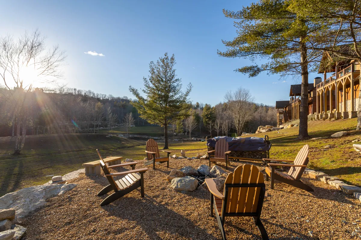 Set in a gravel seating area surrounded by trees, this image presents a circle of Adirondack chairs around a fire pit. The scene is deeply immersed in nature, suggesting memorable evenings spent outdoors, stargazing, or warming up after a day of hiking.